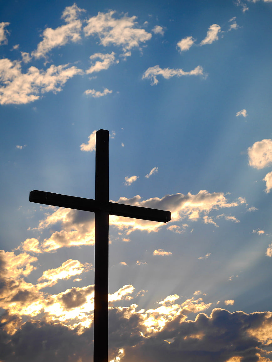 Silhouette of a Cross Against a Dramatic Blue Sky with Sun Rays