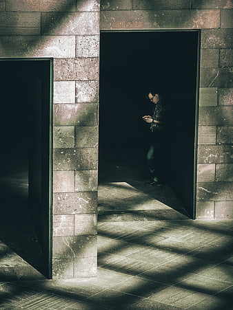 Man standing in shadowed stone doorway using smartphone