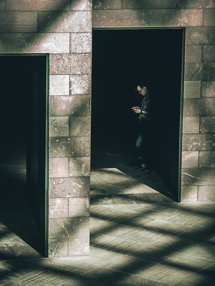 Man standing in shadowed stone doorway using smartphone