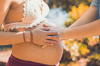 Pregnant woman and partner holding hands on belly outdoors