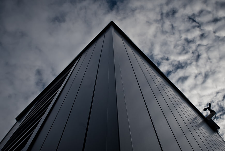 Low angle view of modern dark building against cloudy sky