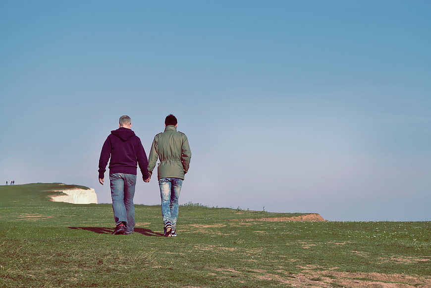 Two men holding hands walking on grassy hill