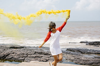 Happy Woman with Yellow Smoke Grenade on Rocky Beach