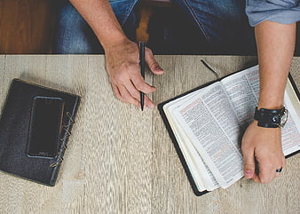 Man Reading Bible with Pen and Smartphone on Wooden Table
