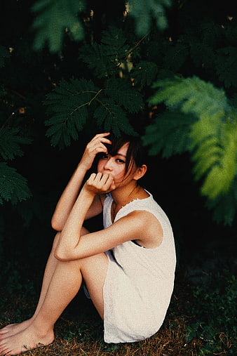 Young woman sitting in dark forest foliage wearing white dress