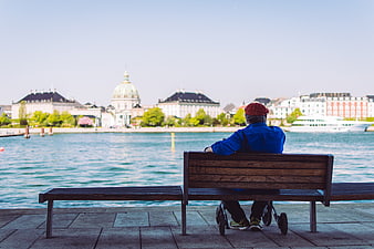Senior man in wheelchair sitting on bench overlooking city waterfront
