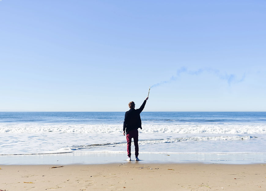 Man Standing on Beach Holding Smoldering Stick