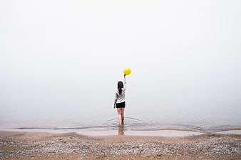 Woman holding yellow balloon on foggy beach