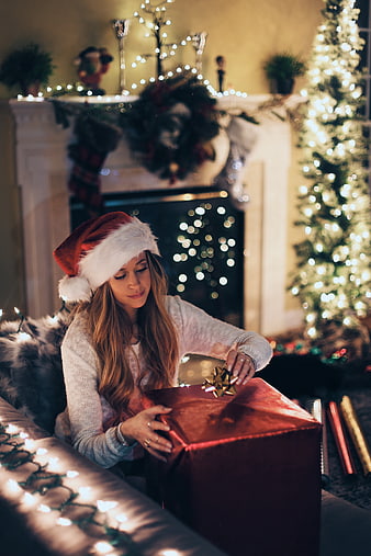 Woman in Santa Hat Opening Christmas Gift by Fireplace