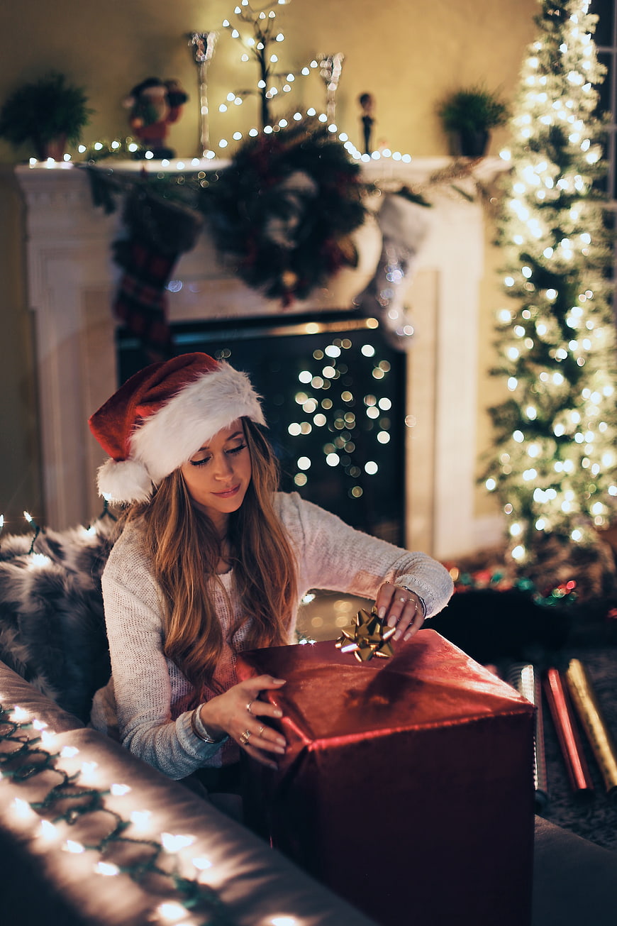 Woman in Santa Hat Opening Christmas Gift by Fireplace