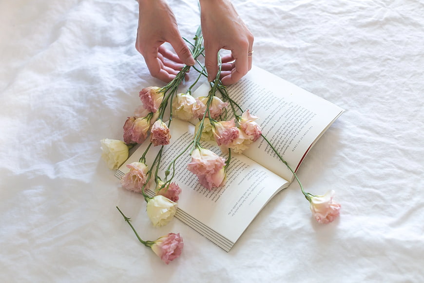 Hands arranging pink and white flowers on an open book