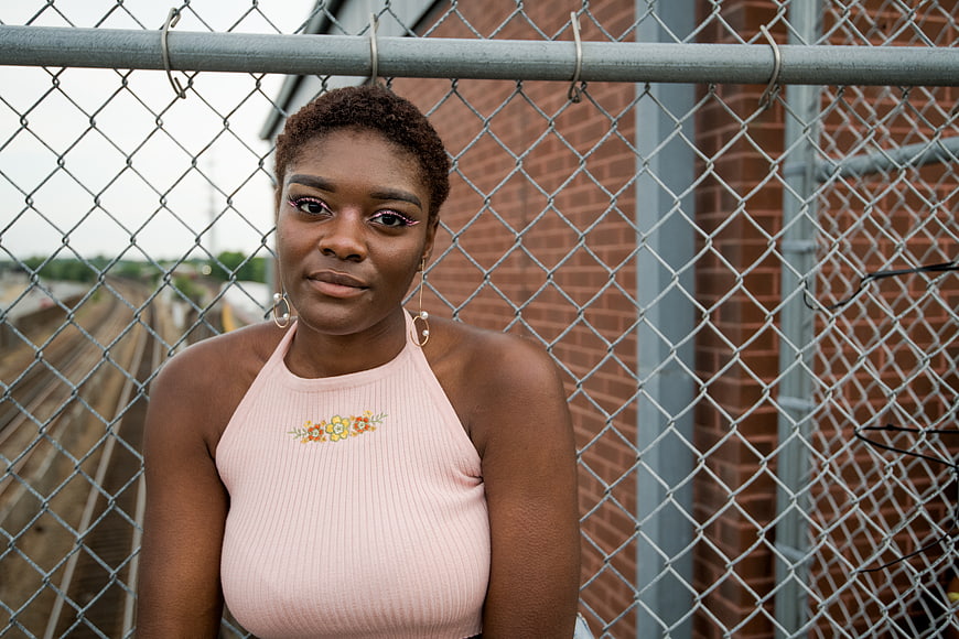 Portrait of young black woman in pink top by chain link fence