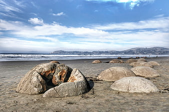 Large smooth boulders on sandy beach with ocean waves and hills