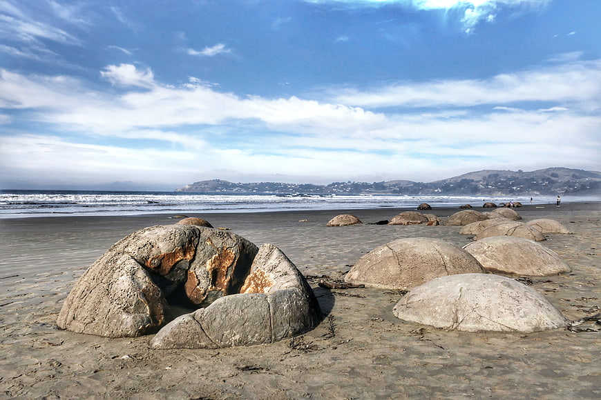 Large smooth boulders on sandy beach with ocean waves and hills