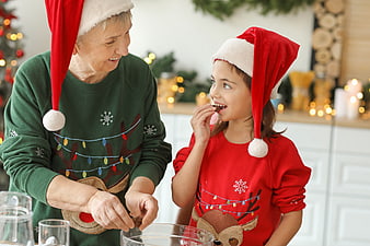 Grandmother and granddaughter baking Christmas cookies in festive sweaters