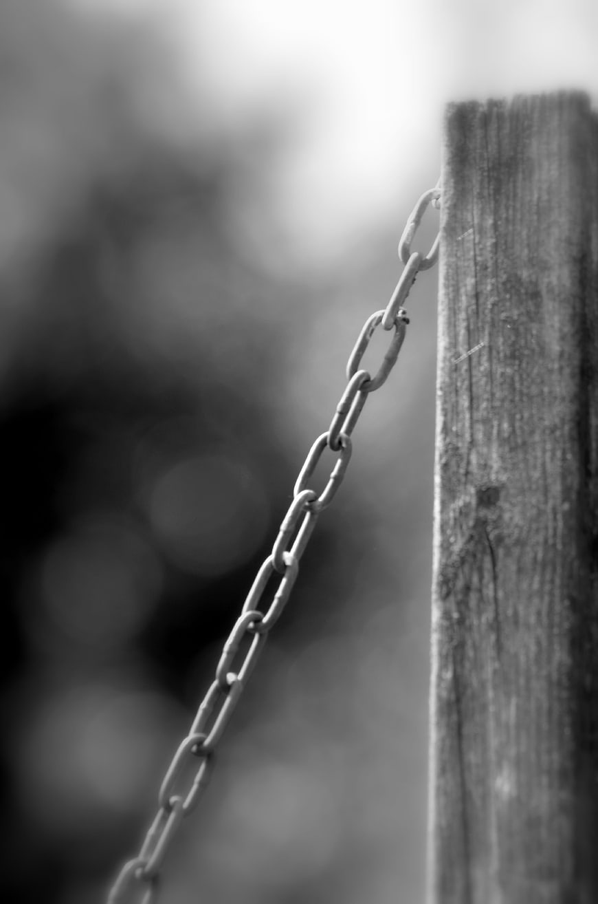 Black and white close-up of metal chain on wooden post