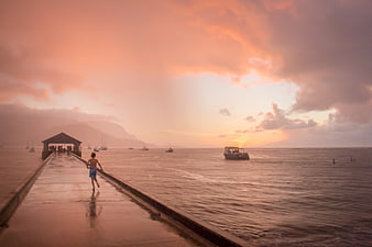 Boy Running on Wet Pier at Sunset with Boats