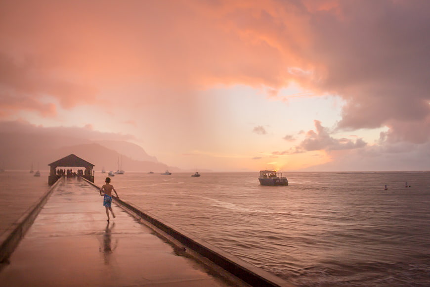 Boy Running on Wet Pier at Sunset with Boats