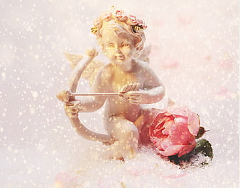 Cupid statue with bow and arrow beside pink rose in falling snow