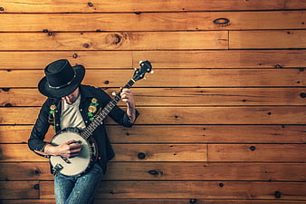 Man in cowboy hat playing banjo against wooden wall