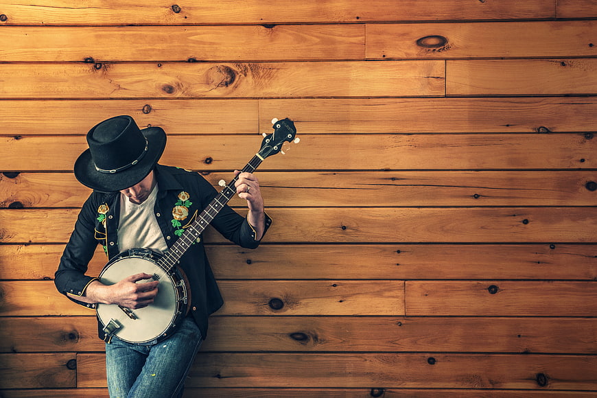 Man in cowboy hat playing banjo against wooden wall