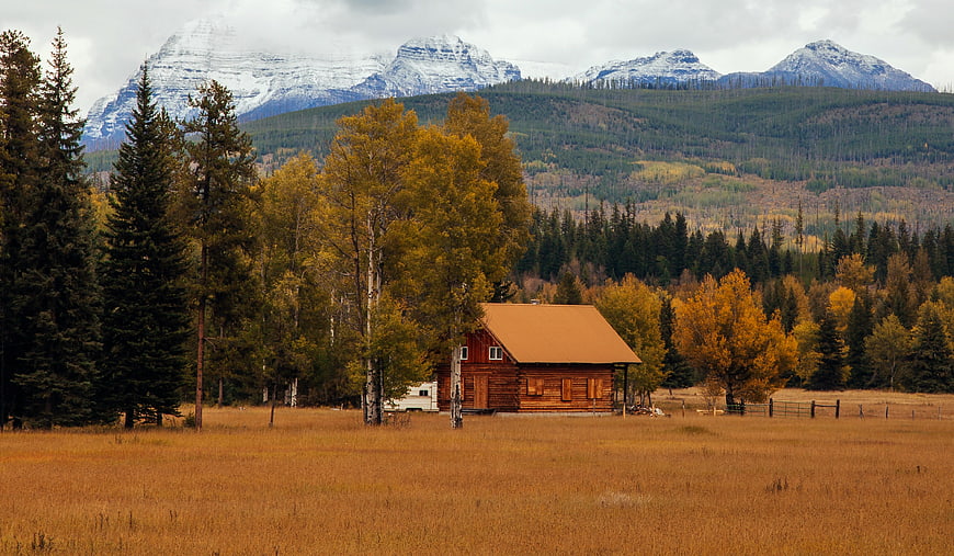 Rustic Cabin in Golden Autumn Meadow with Snowy Mountains