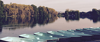 Row of green boats on calm lake with autumn trees
