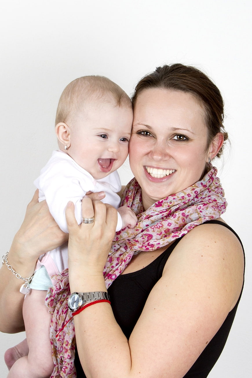 Smiling Mother Holding Happy Baby Girl Against White Background