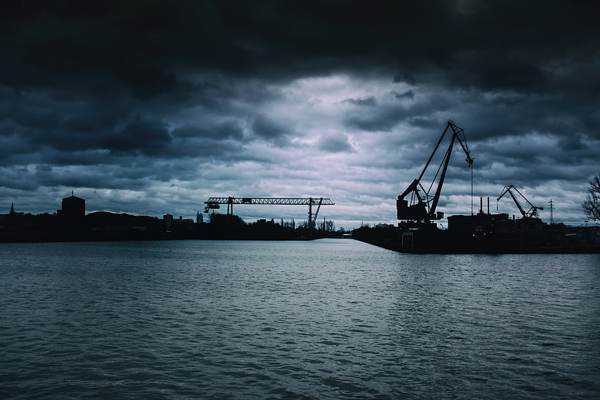 Silhouette of industrial cranes at a port under stormy sky