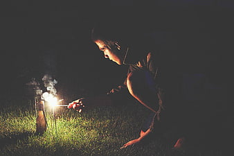Man lighting firework bottle in grass at night
