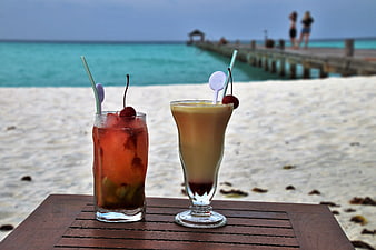 Tropical cocktails on a wooden table with a beach and pier background