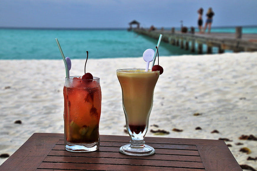 Tropical cocktails on a wooden table with a beach and pier background