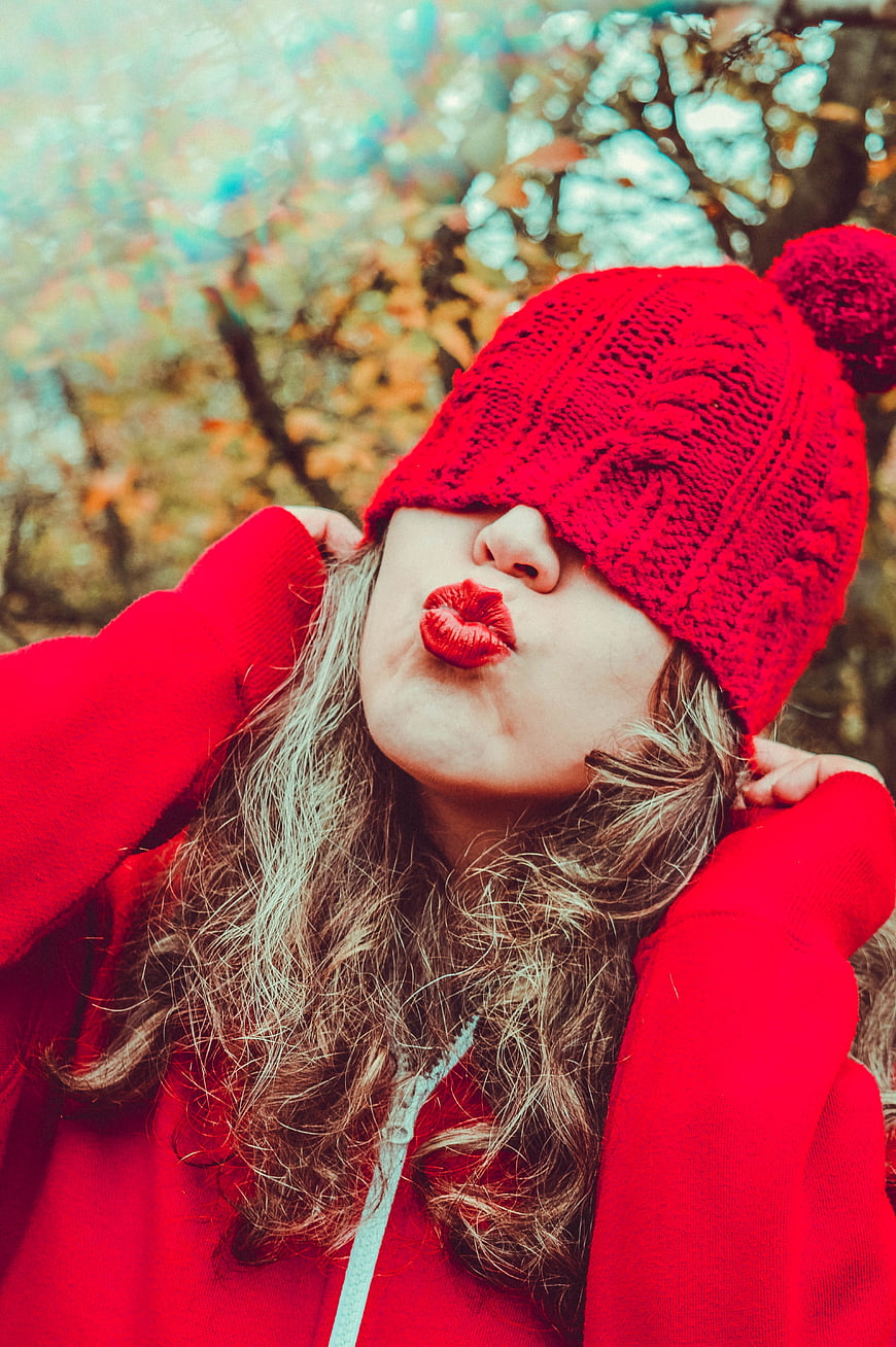 Playful woman in red knit hat blowing kiss outdoors