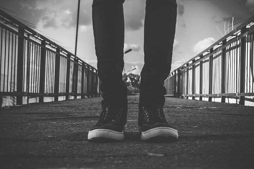 Low angle black and white photo of sneakers on a bridge