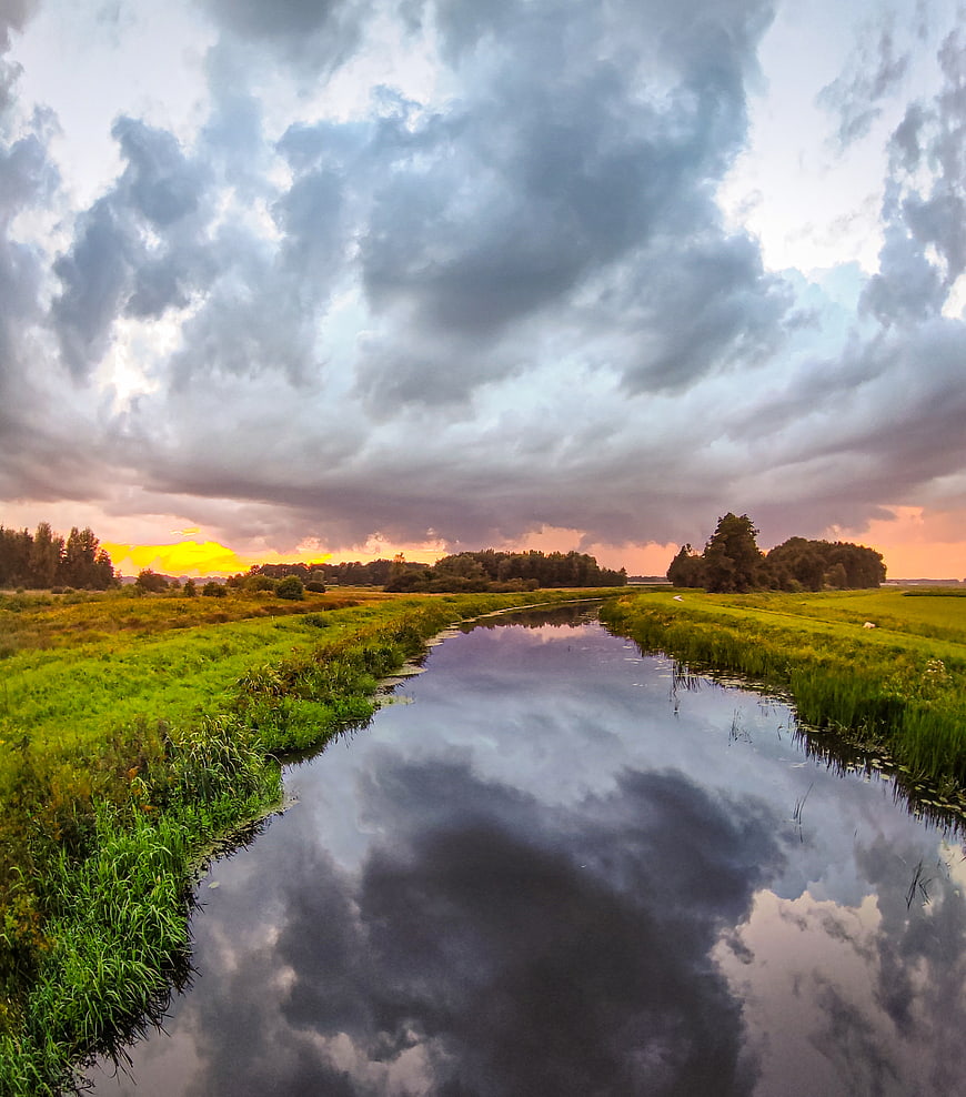 Dramatic sunset clouds reflected in a winding river through green meadows