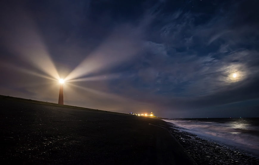 Lighthouse Beam at Night on Dark Beach with Moon