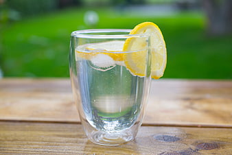 Refreshing glass of lemon water on wooden table outdoors