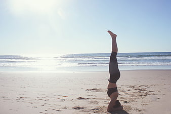 Woman doing headstand yoga on sunny beach