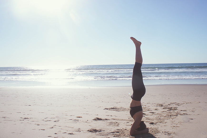 Woman doing headstand yoga on sunny beach
