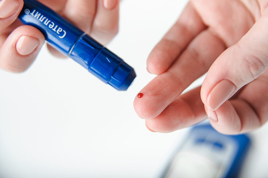 Close-up of hands using a blue lancet pen for a blood glucose test