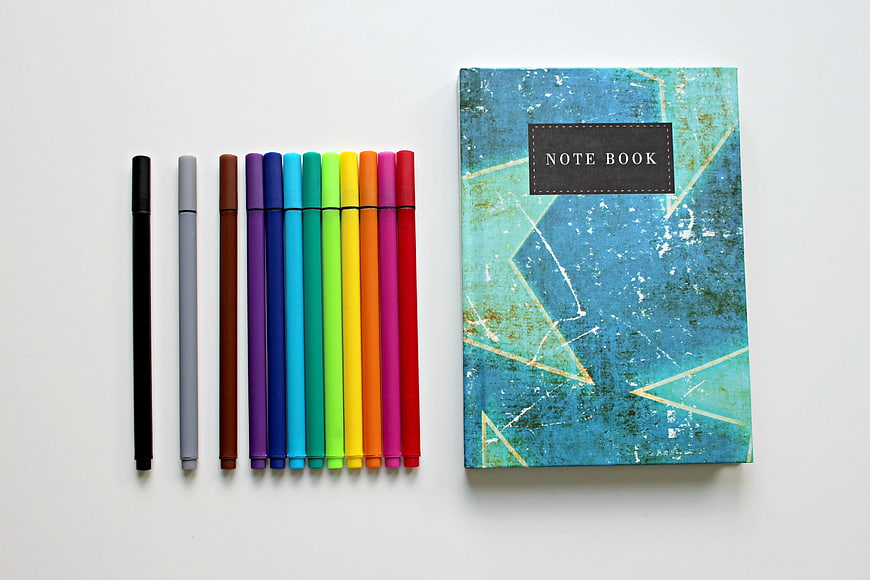 Colorful pens and blue notebook on white background