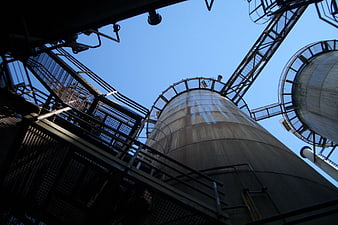 Low angle view of industrial steel silos against blue sky