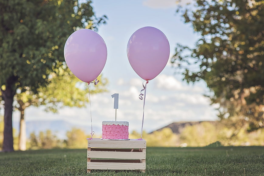First Birthday Cake with Pink Balloons on Wooden Crate Outdoors