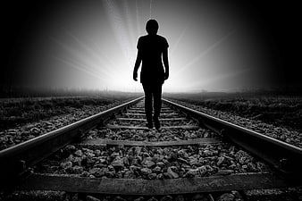 Silhouette of a person walking on railroad tracks toward bright light
