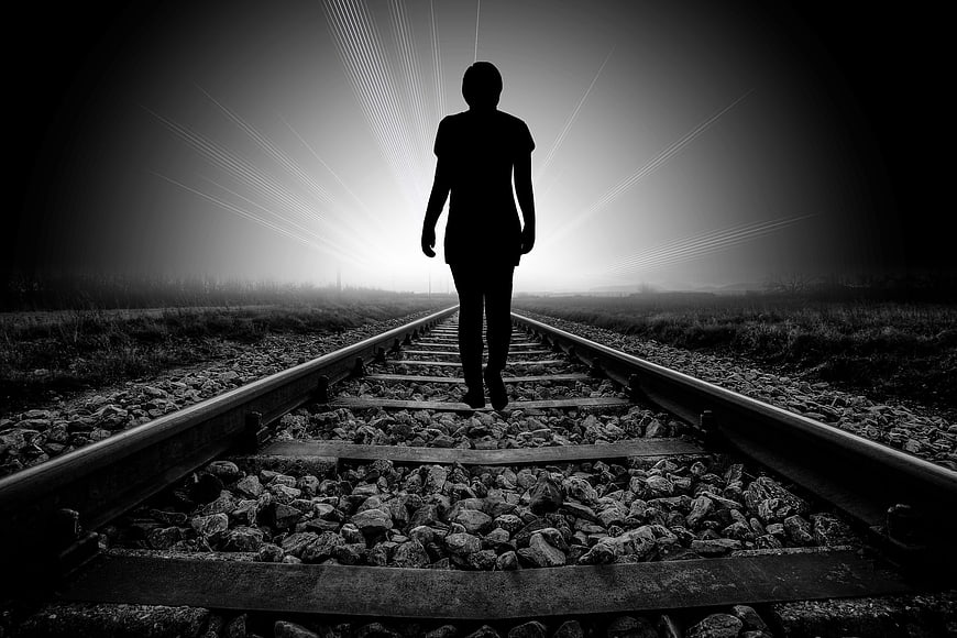 Silhouette of a person walking on railroad tracks toward bright light