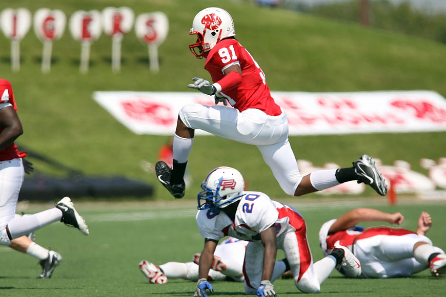 American football player leaping over opponent during game