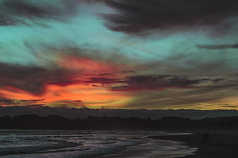 Dramatic Sunset Over Ocean Beach with Silhouetted Figures