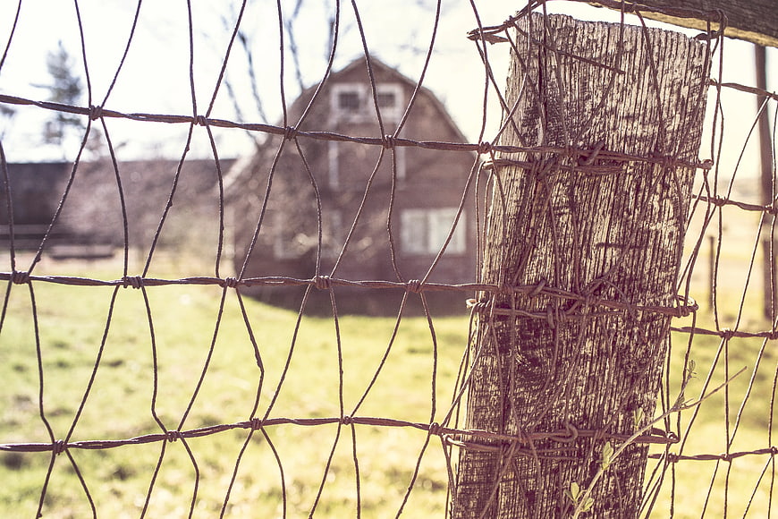 Closeup of Rusty Wire Fence with Barn in Background