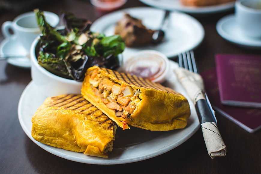 Grilled breakfast burrito with salad and coffee on wooden table