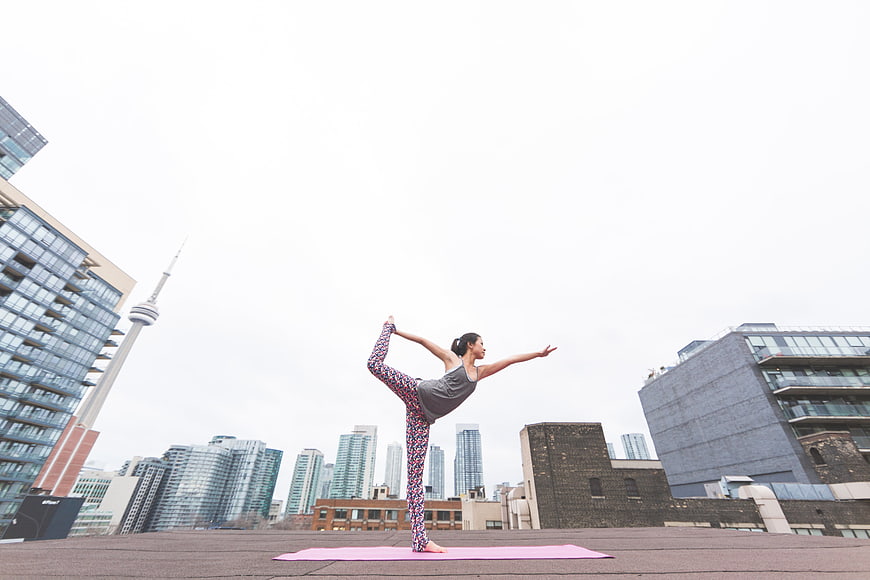 Woman doing yoga on rooftop with city skyline background